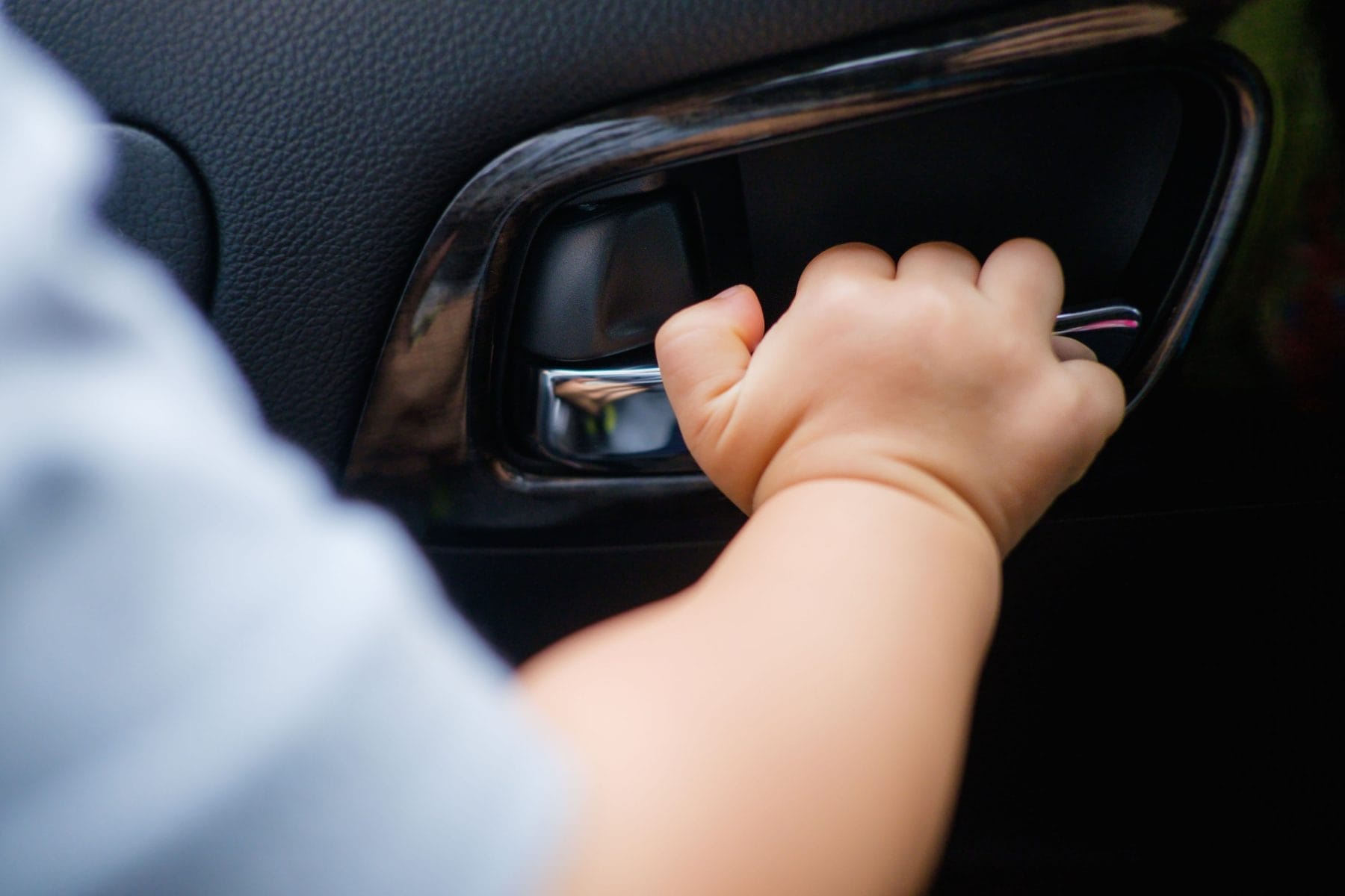 Little Asian 18 months / 1 year old baby boy child holding on to the door handle inside of the car, kid try to open the car door, Child safety concept