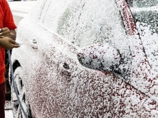 Detergent soap foam known as snow wash sprayed onto car at garage before washing