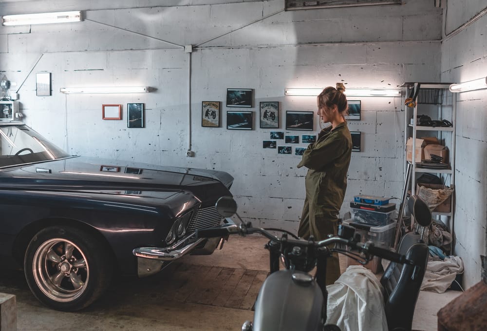 Attractive Caucasian woman looking at her vintage old car in a garage