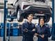 Auto car repair service center. Two happy mechanics - man and woman standing by the car